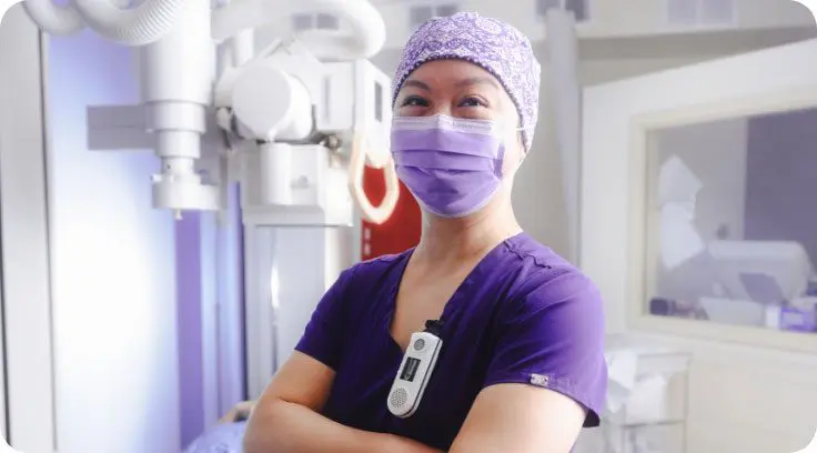 A woman in a hospital hallway wearing a purple mask, hair scarf and scrubs