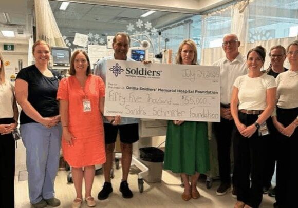 Sandra Schmirler 2025 A group of female nurses stand in a Neonatal Intensive Care Unit with a large cheque.