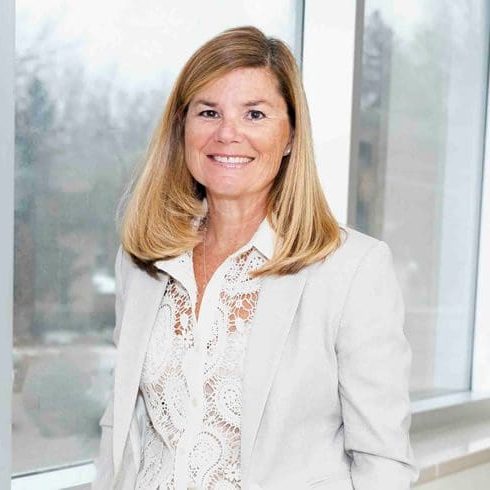 A woman in white jacket standing next to window.